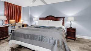 A bedroom with a bed, two bedside tables with lamps, a desk with a chair, a ceiling fan, and a window with curtains. - Unobstructed Oceanfront View! 3BR, 3BA, Grand Atlantic Resort, 20th Floor Condo (Myrtle Beach)