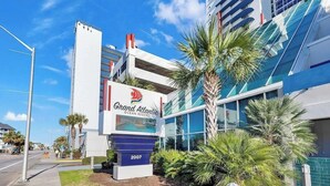 A hotel with a prominent sign for Grand Atlantic Ocean Resort, featuring a modern building with glass windows and a palm tree in the foreground. - Unobstructed Oceanfront View! 3BR, 3BA, Grand Atlantic Resort, 20th Floor Condo (Myrtle Beach)