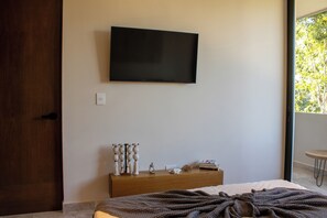 Ein Schlafzimmer mit einem Bett, einer Holzkommode, einem flachbildfernseher an der Wand und einem Fenster mit Blick auf Bäume.