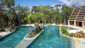 Uma área de piscina com duas piscinas interligadas, rodeada por vegetação exuberante e um edifício moderno.