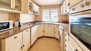 Uma cozinha com armários brancos, forno embutido, micro-ondas e janela que proporciona luz natural.