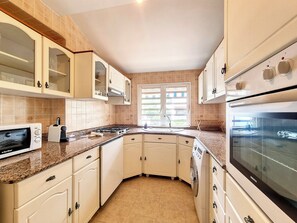 A kitchen with white cabinets, a built-in oven, a microwave, and a window providing natural light. - Le Mosala 5 - Climatisation - Vue mer (Saint-Leu)