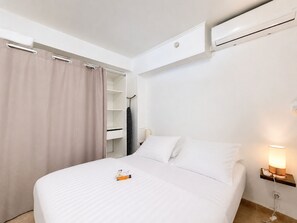 A hotel room with a bed, a bedside table with a lamp, a wardrobe, and an air conditioning unit.