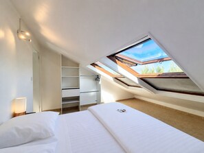 A bedroom with a skylight, a bed, a bedside table, and a wardrobe.