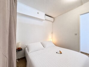 A bedroom with a bed, an air conditioning unit, a bedside lamp, and a door. - Le Mosala 5 - Climatisation - Vue mer (Saint-Leu)