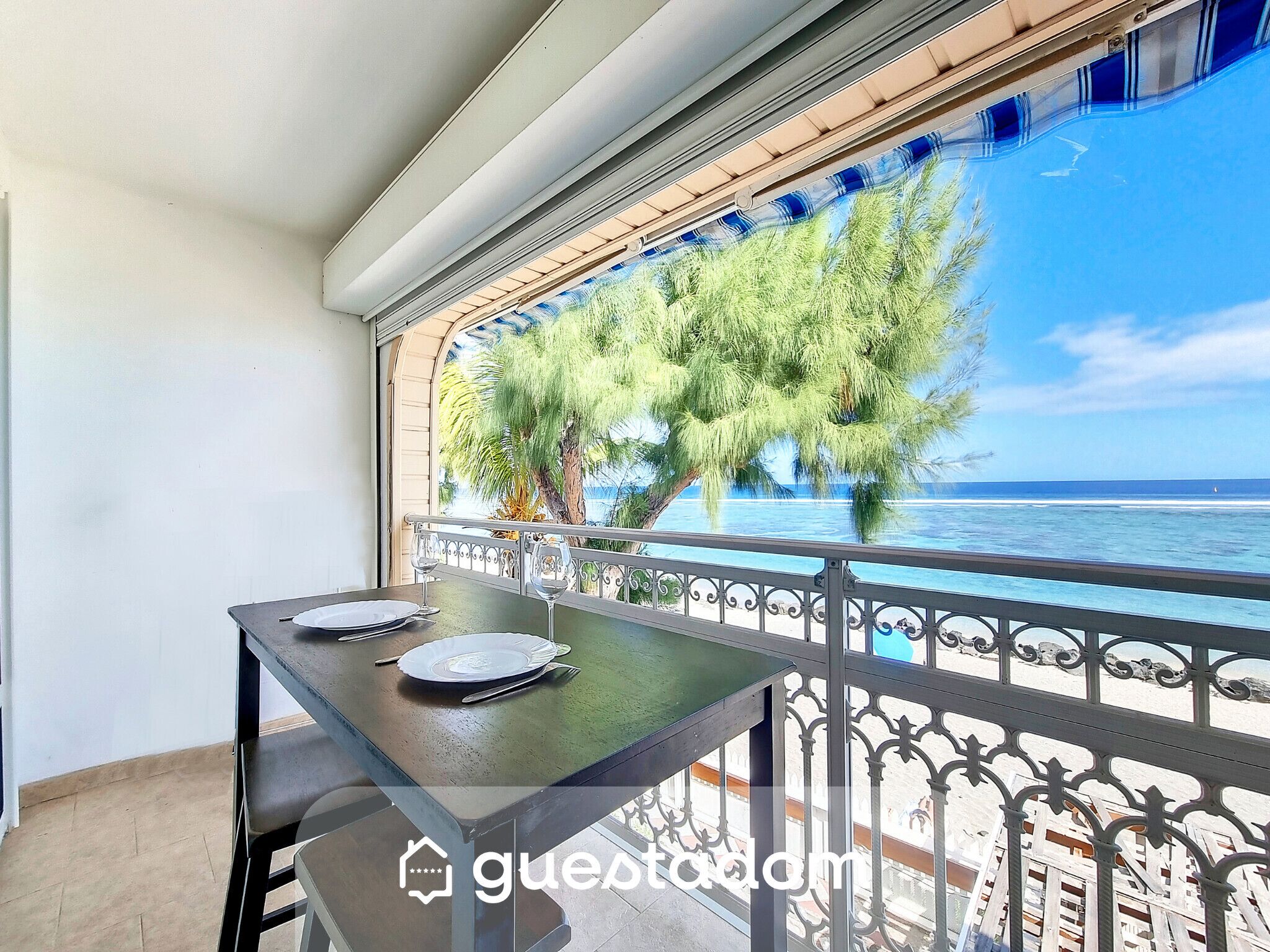 Ein Balkon mit Esstisch, der auf einen Strand und das Meer blickt.