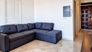 Een moderne woonkamer met een hoekbank, een houten deur en een betegelde vloer.