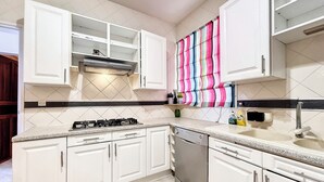 Een keuken met witte kastjes, een gasfornuis, een vaatwasser, en een kleurrijke gestreepte handdoek aan de muur.