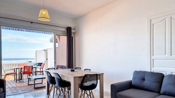 Een moderne woonkamer met een eethoek, een grijze bank en uitzicht op zee.