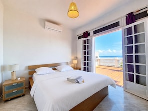 A hotel room with a bed, a nightstand, a lamp, and a view of the sea through a glass door. - Le Mosala 2 - Climatisation - Vue mer (Saint-Leu)