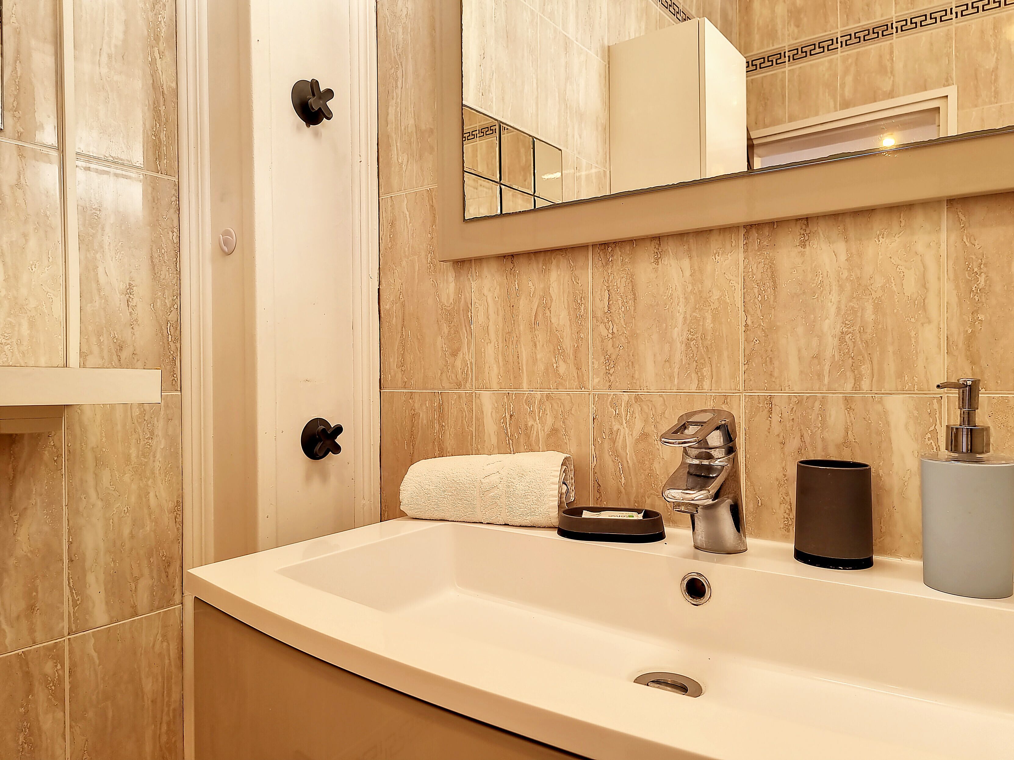 A bathroom with a white sink, a towel, a soap dispenser, and a mirror.