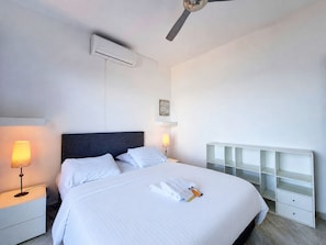 Ett hotellrum med en säng, sänglampor, en luftkonditioneringsanläggning, en takfläkt och en inbyggd hyllsektion.