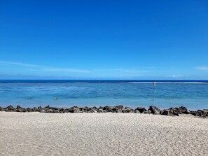 Una playa con agua azul cristalina, costa rocosa y un faro a lo lejos.
