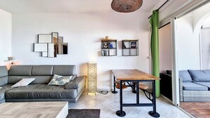 Ein modernes Wohnzimmer mit einem grauen Sofa, einem Holztisch, einem Esstisch mit Stühlen und einer hängenden Leuchte.