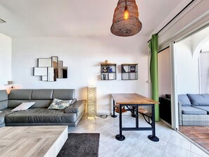 Ett modernt vardagsrum med en grå soffa, ett soffbord i trä, ett matbord med stolar och en hängande lampa.