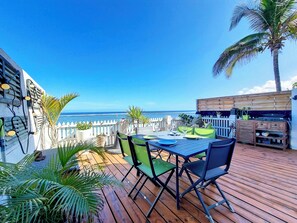 Un patio exterior con cubierta de madera, una mesa con sillas y vista al océano.