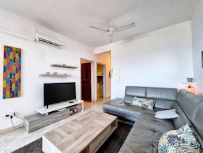 Una sala moderna con televisor de pantalla plana, un sofá gris, una mesa de centro de madera y un ventilador de techo.