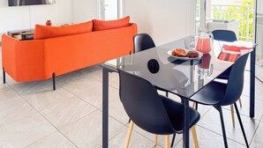 Ein modernes Wohnzimmer mit einem Glastisch, schwarzen Stühlen und einem orangefarbenen Sofa.