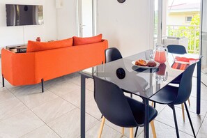 Ein modernes Wohnzimmer mit einem Glastisch, schwarzen Stühlen und einem orangefarbenen Sofa.