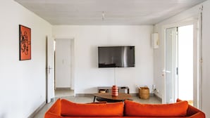 Ein modernes Wohnzimmer mit einer Couch, einem flachbildfernseher an der Wand und einem Essbereich mit Tisch und Stühlen.