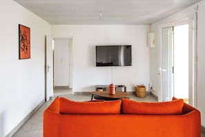 Ein modernes Wohnzimmer mit einer Couch, einem flachbildfernseher an der Wand und einem Essbereich mit Tisch und Stühlen.