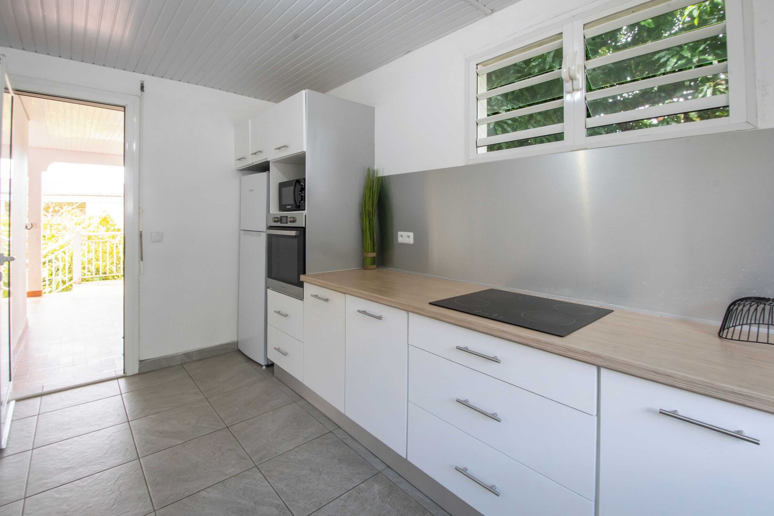 A kitchen with white cabinets, a countertop, a microwave, an oven, and a window with green foliage.