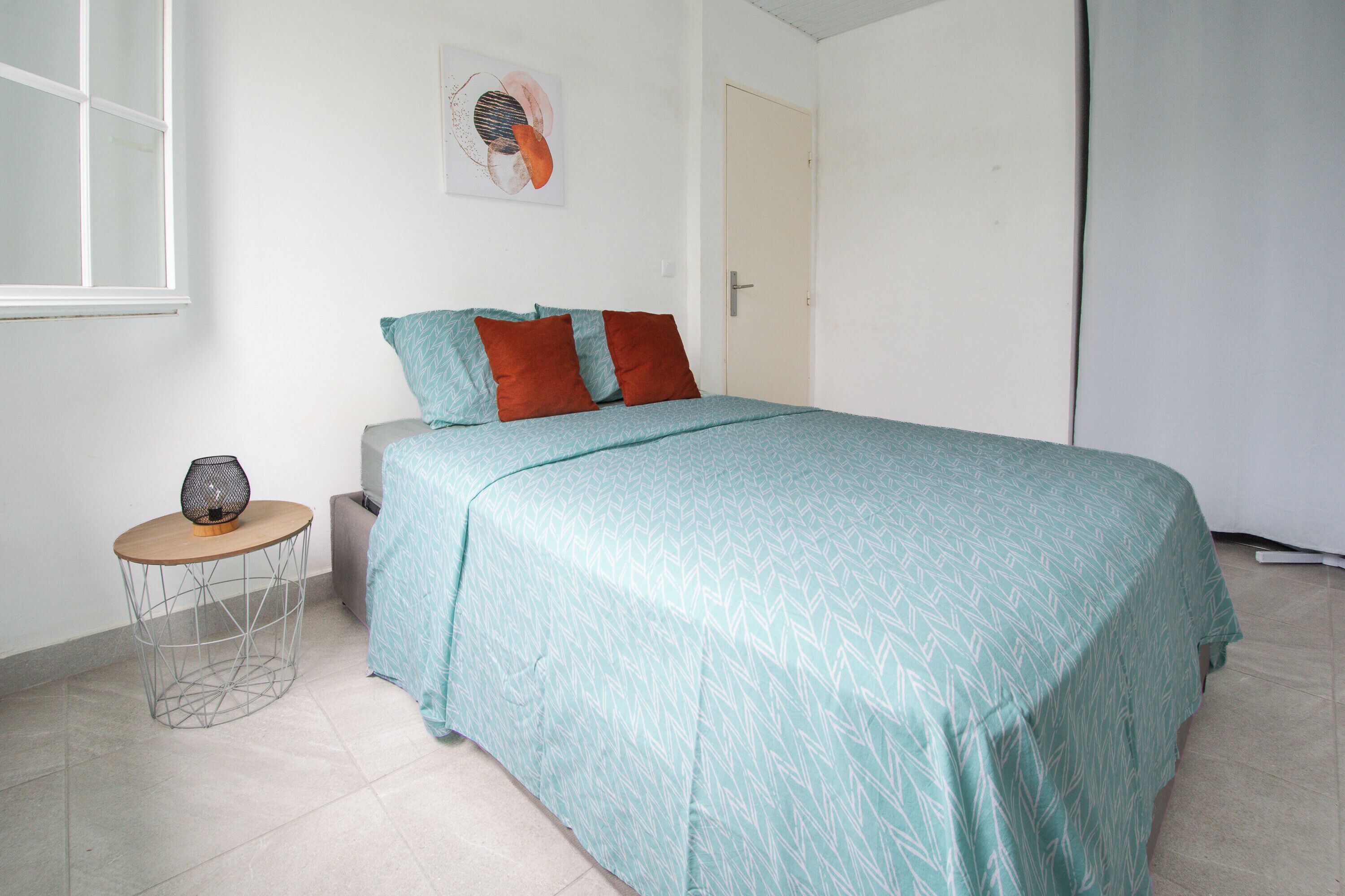 Een slaapkamer met een bed, een klein rond tafeltje met een lamp en een deur.