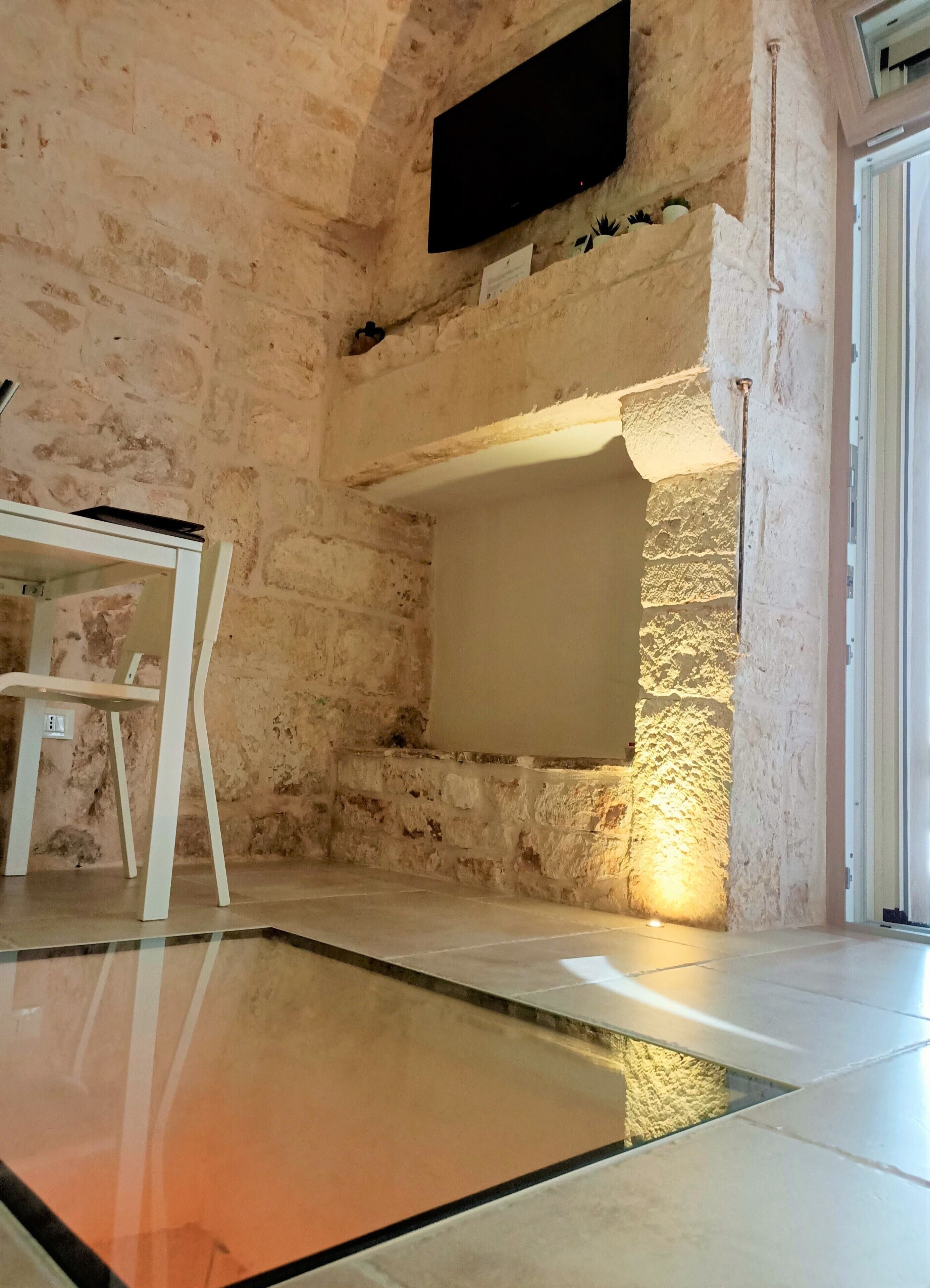 A room with a stone wall, a flat-screen TV mounted on it, a white chair, and a tiled floor.