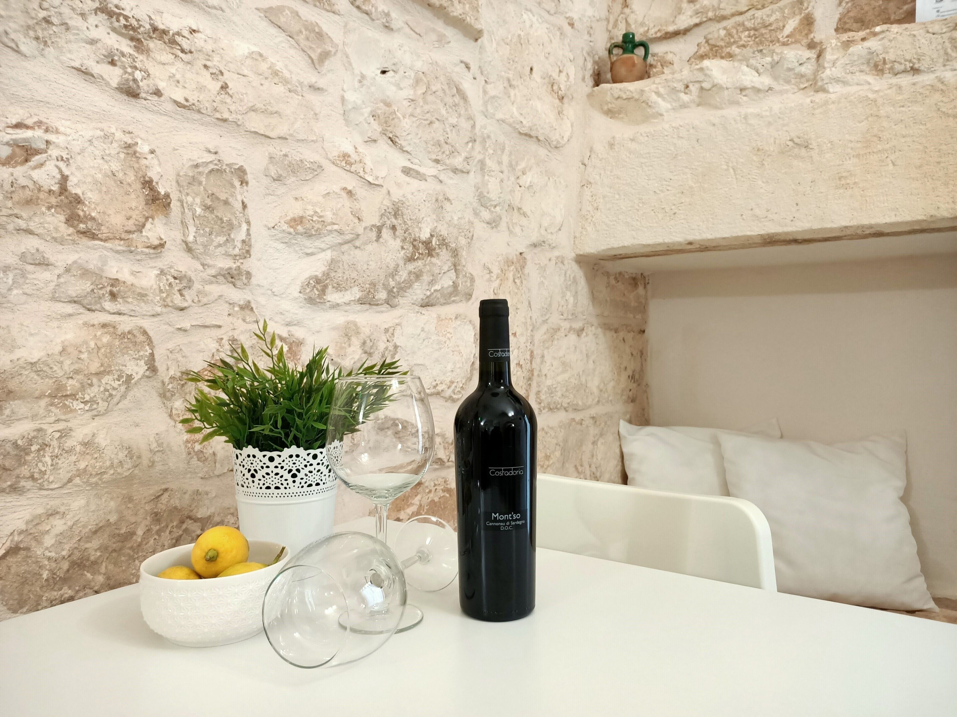 A table with a bottle of wine, a glass, a bowl of lemons, and a potted plant.