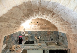 Une cuisine dotée d’un plafond en forme d’arc en pierre, de carreaux décoratifs, d’une machine à café moderne et d’un évier.