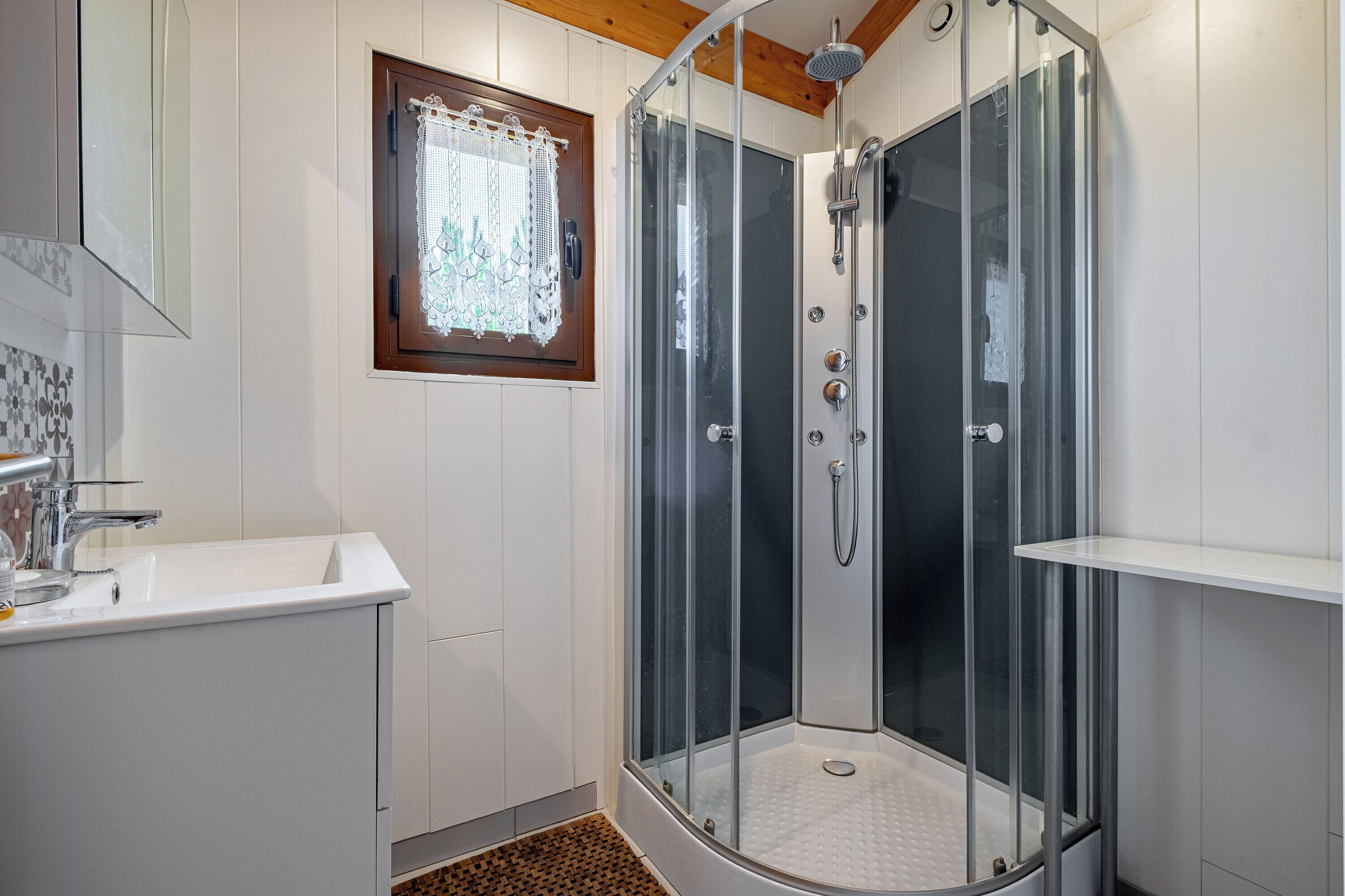A modern bathroom with a glass-enclosed shower, a white sink, and a wooden ceiling.