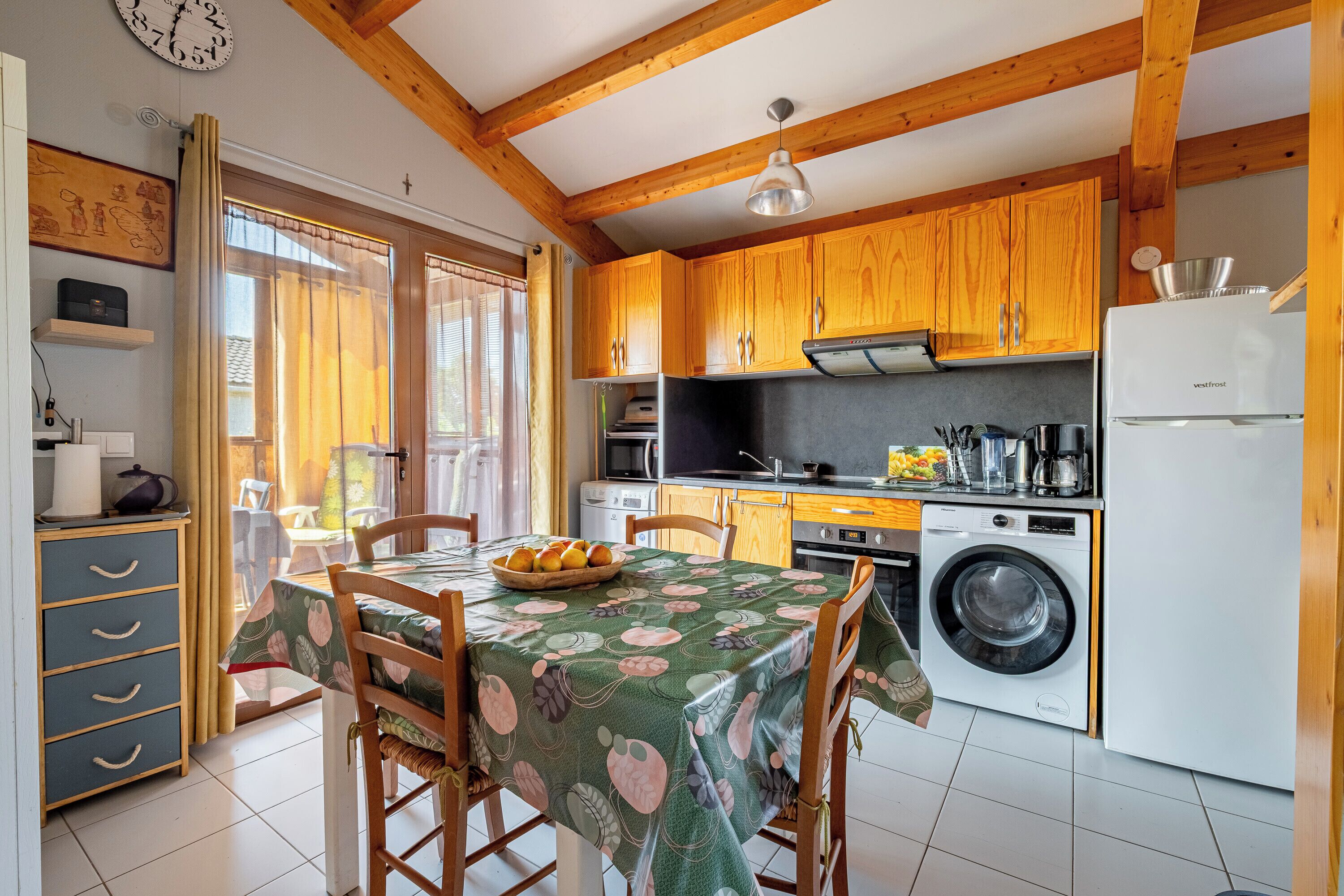 Cocina compacta con armarios de madera, lavadora y comedor con una mesa para dos.