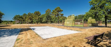 Une aire de jeux dotée d’une zone de jeux en béton, de bancs et d’un terrain de basket-ball clôturé.
