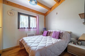 A bedroom with a bed, a window with curtains, a bedside table, and a wall clock. - Le Téno - Nature et détente - Wifi (Marzan)