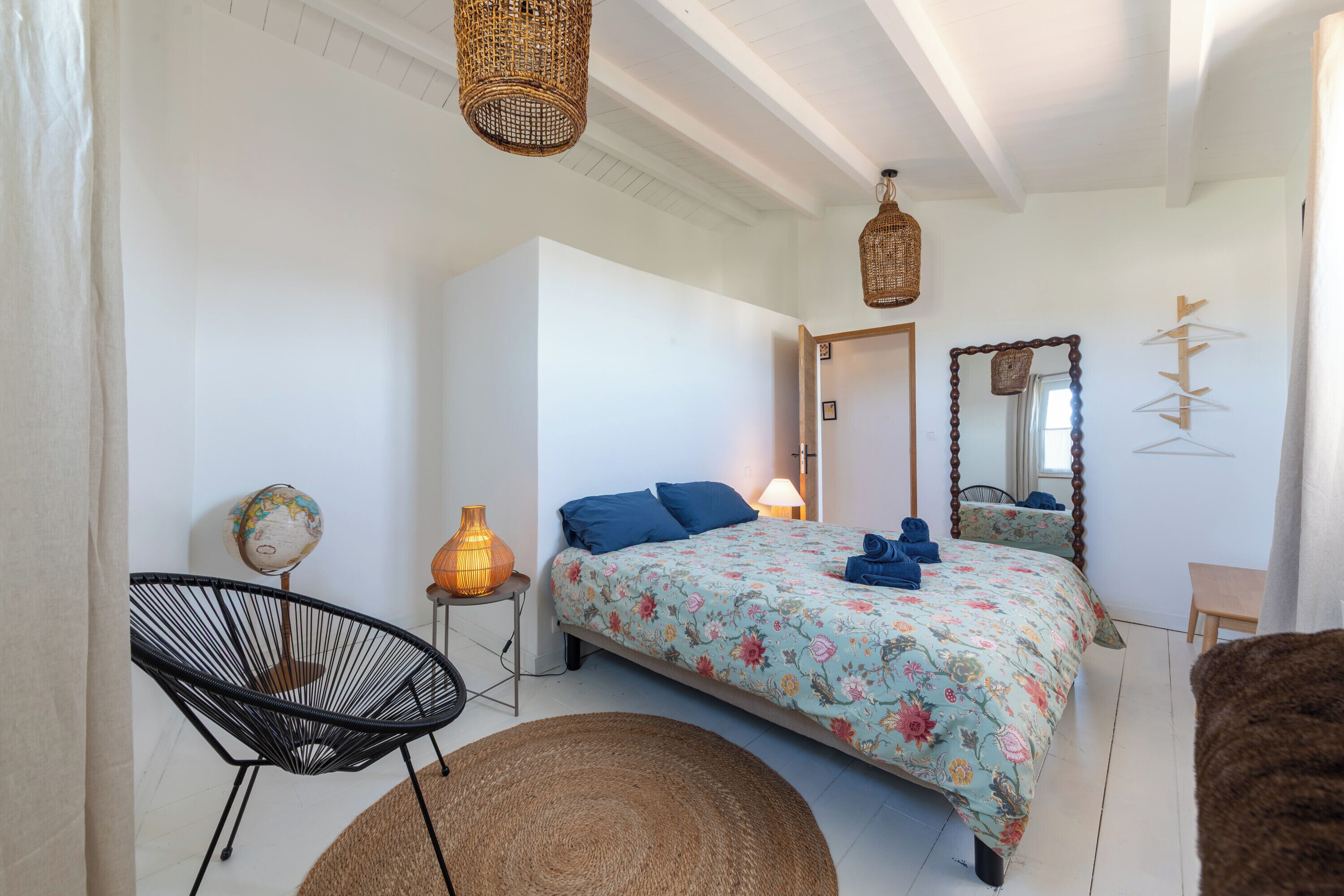 A bedroom with a bed, a chair, a globe, a lamp, and a mirror.