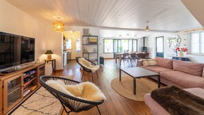 A spacious living area with a television, seating, and a dining area visible through an open door. - Villa Insula - Proche plage - Jardin (Les Portes-en-Ré)