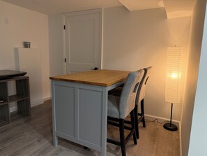Un comedor con mesa de madera y sillas tapizadas en gris, una puerta blanca y una lámpara de pie.