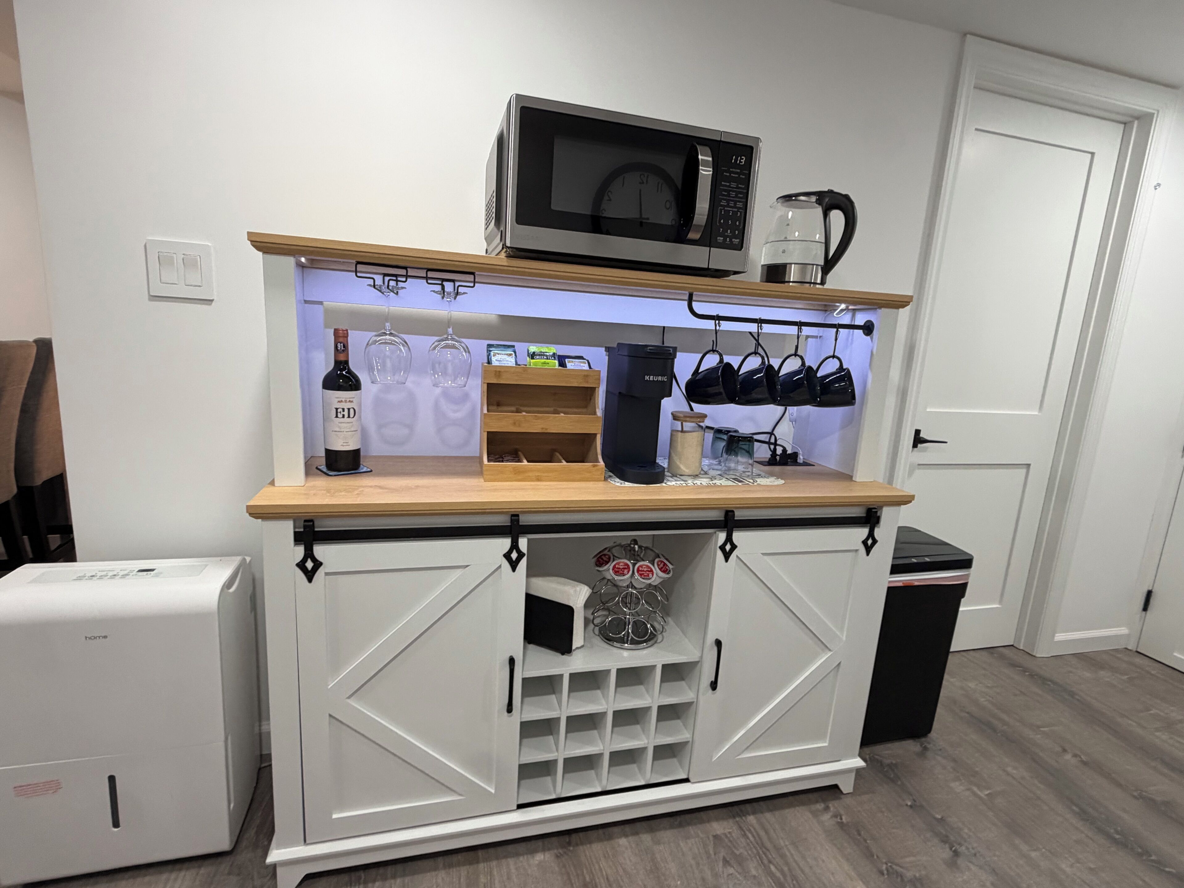A kitchenette with a microwave, coffee maker, wine bottle, and wine glasses.