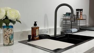 Een keuken met een zwarte kraan, een zeepdispenser, een vaas met schelpen en een bloemstuk.