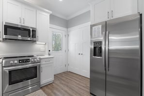 Una cocina moderna con electrodomésticos de acero inoxidable, armarios blancos y piso de madera.