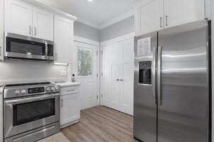Una cocina moderna con electrodomésticos de acero inoxidable, armarios blancos y piso de madera.