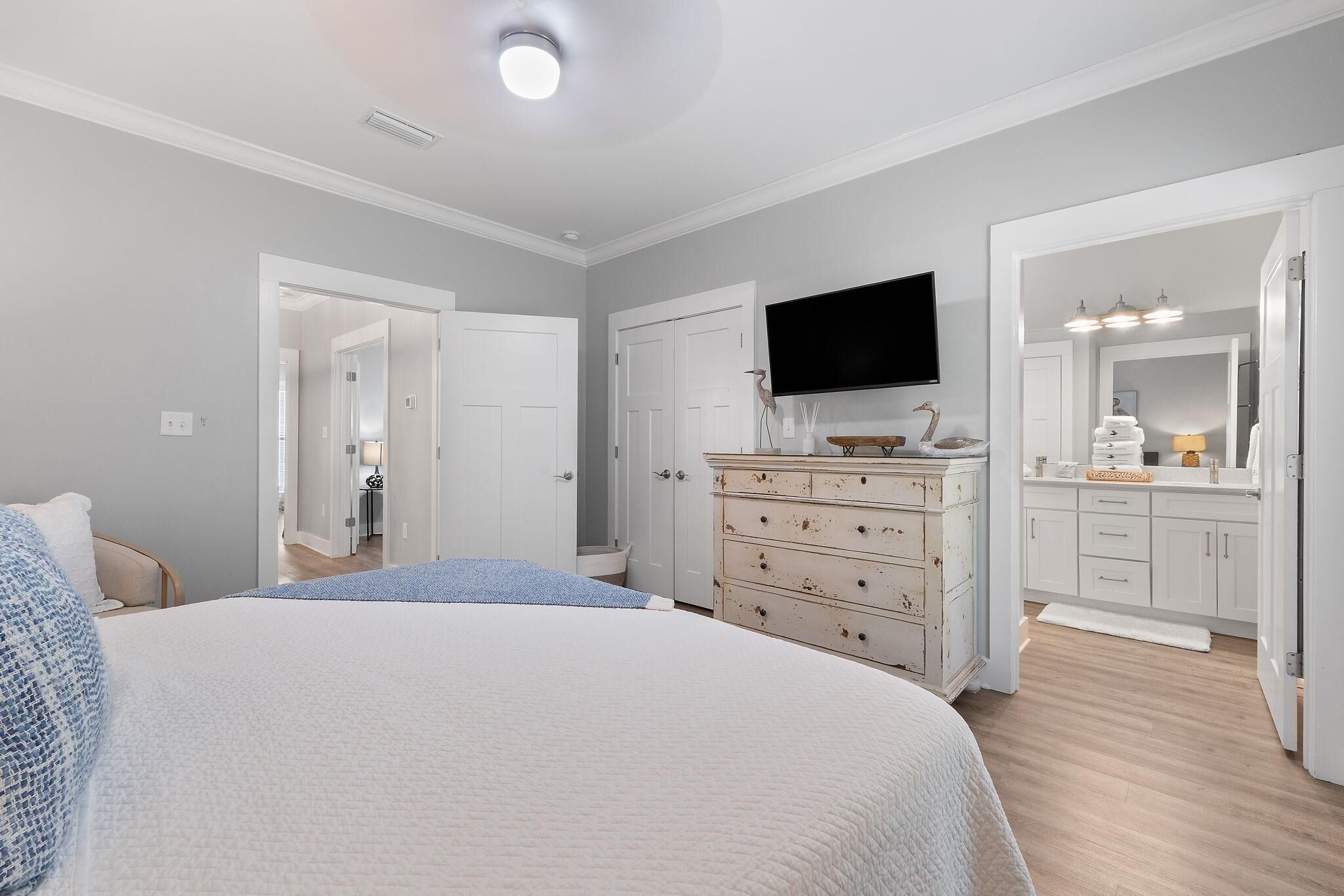 A bedroom with a large bed, a dresser, a television, and a bathroom with a mirror and sink.