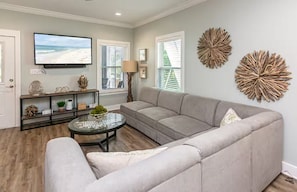 Ein Wohnzimmer mit grauem Sofa, Couchtisch, Flachbildfernseher und Wanddekoration.