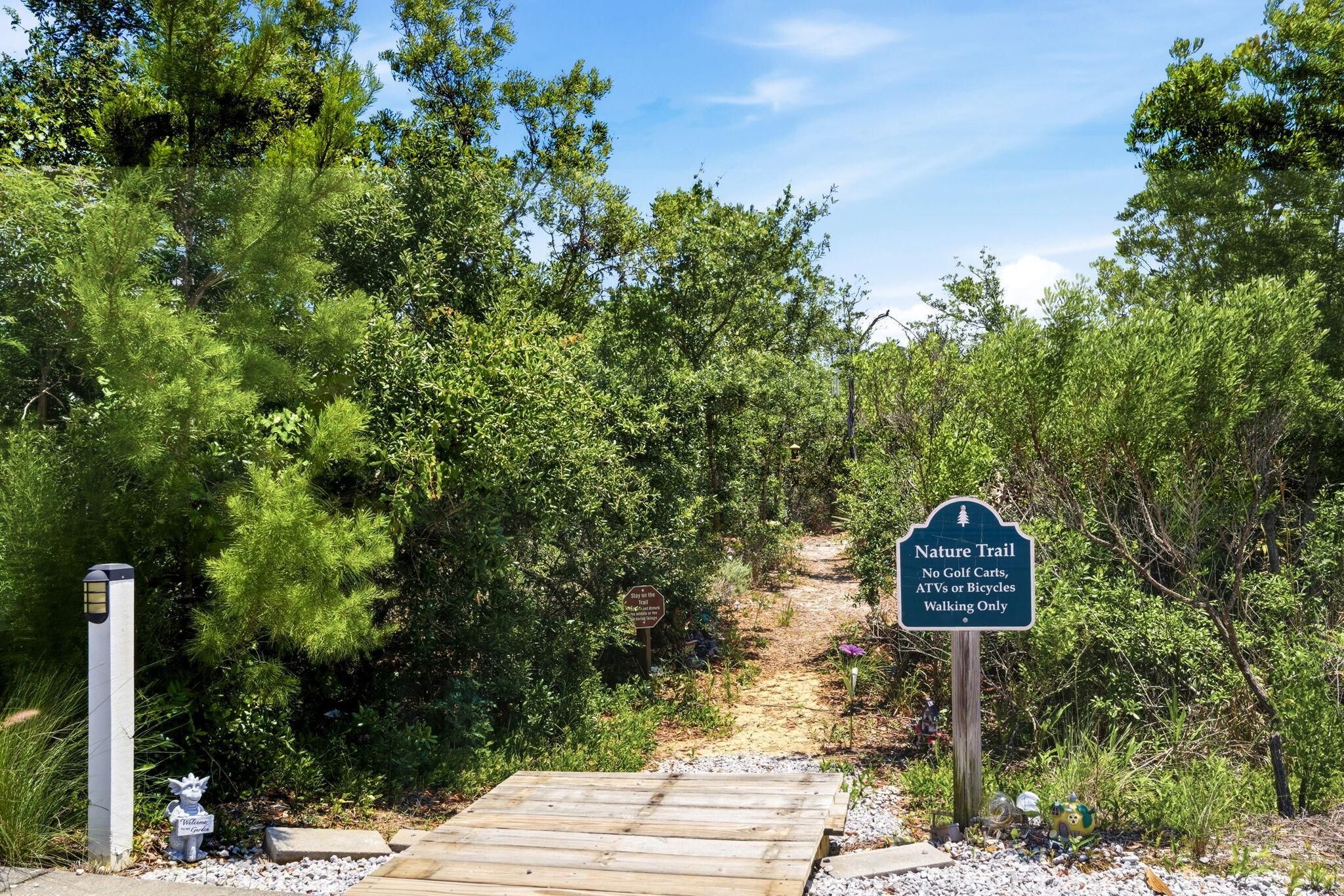 A nature trail sign, a wooden pathway, and surrounding greenery.