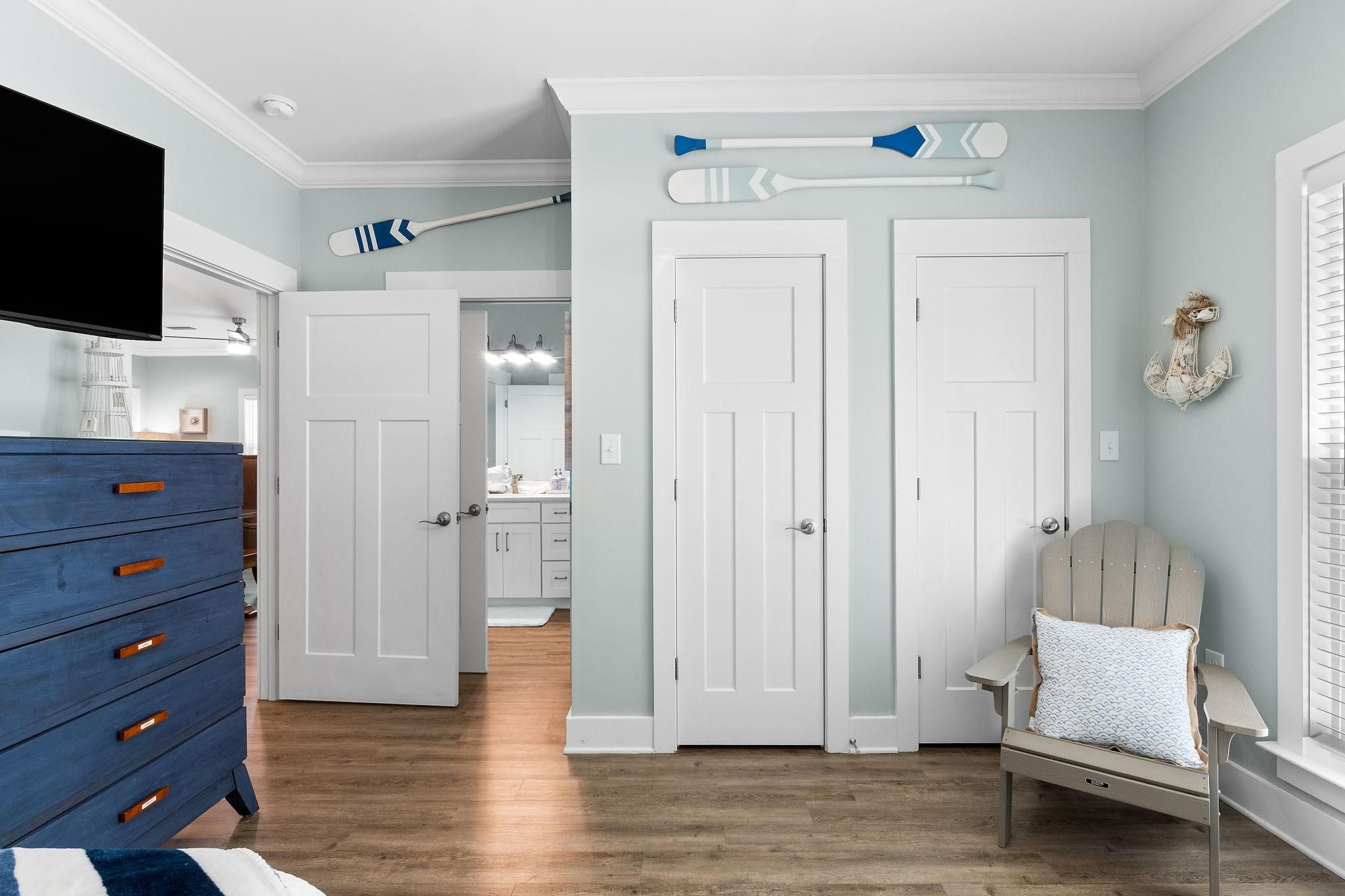 A room with a blue dresser, two white doors, a bed with a white pillow, and a wall-mounted TV.