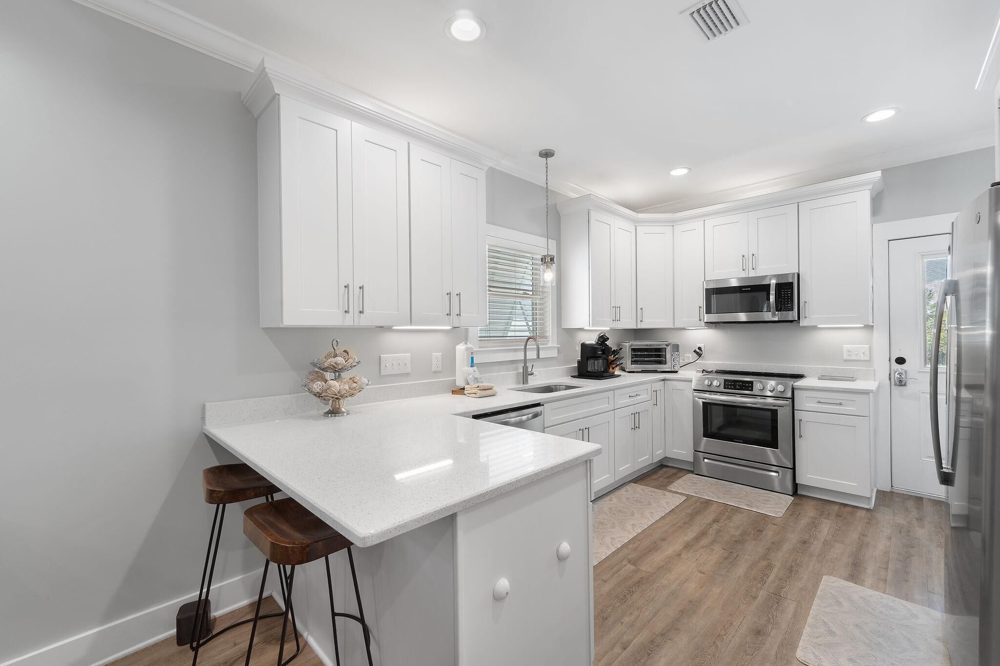 Una cocina moderna con armarios blancos, una isla central con taburetes, microondas, horno y refrigerador.