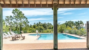 A covered outdoor swimming pool with lounge chairs and a picnic table, surrounded by trees and greenery.