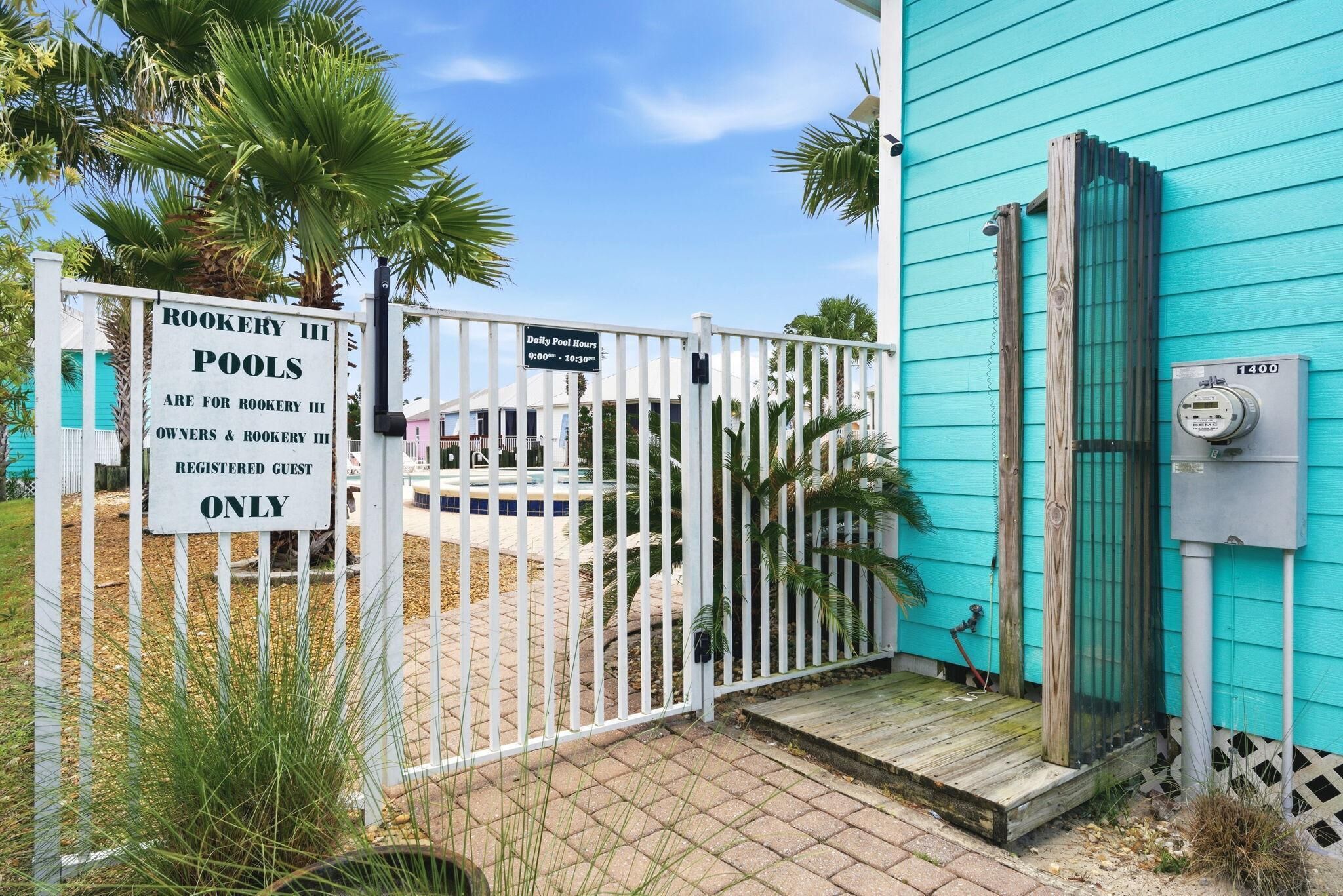 A gated entrance to a pool area with a sign indicating pool hours and a utility box.