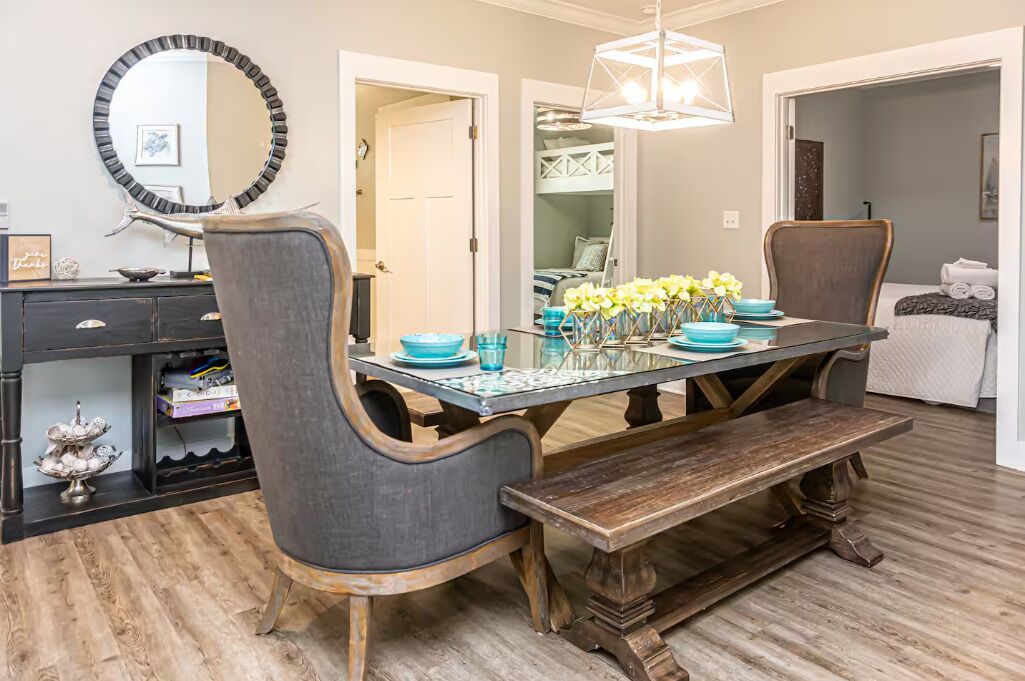 A dining area with a table set for four, surrounded by chairs, a bench, and a decorative mirror.