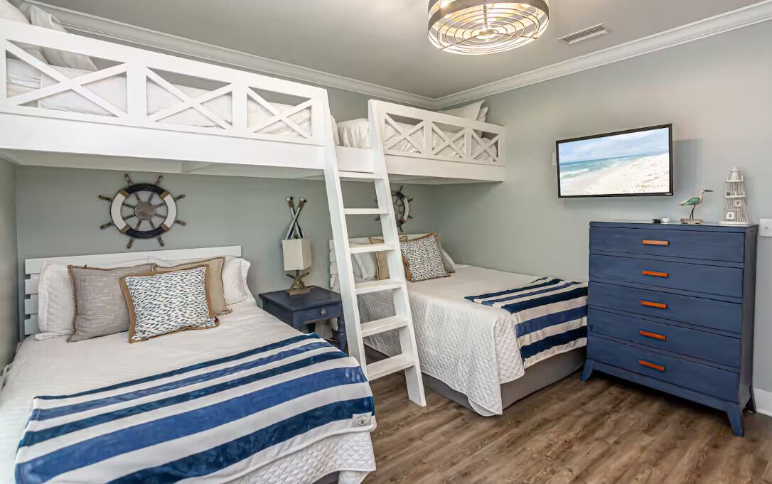 A bedroom with bunk beds, a dresser, a television, and nautical-themed decor.